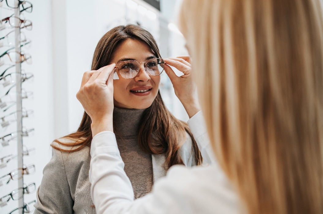 Modische Frau bei der Auswahl eines Brillengestells in einem Optikgeschäft.